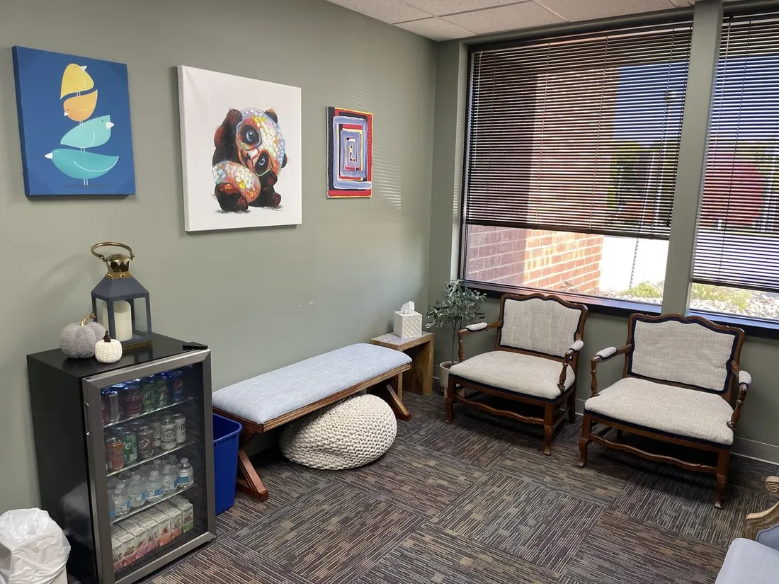 Waiting area with a cushioned bench, chairs, refreshments, and warm artwork